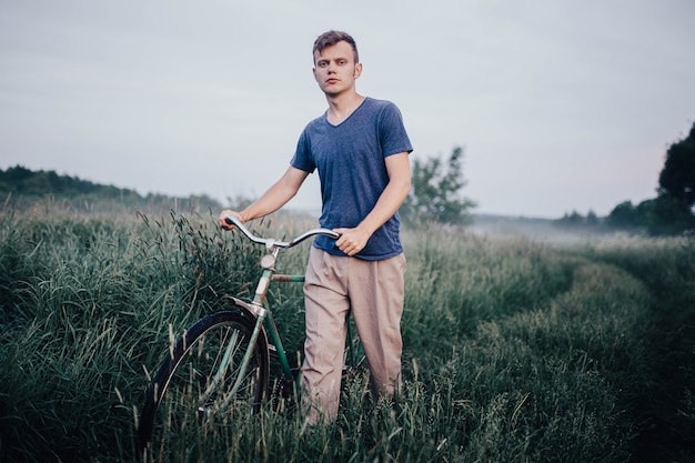 l'uomo cammina con una bicicletta retrò verde su una strada di campo ed erba in estate