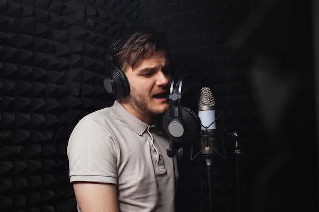 L'uomo canta nel microfono, le cuffie dello studio di registrazione professionale, le pareti nere e morbide.