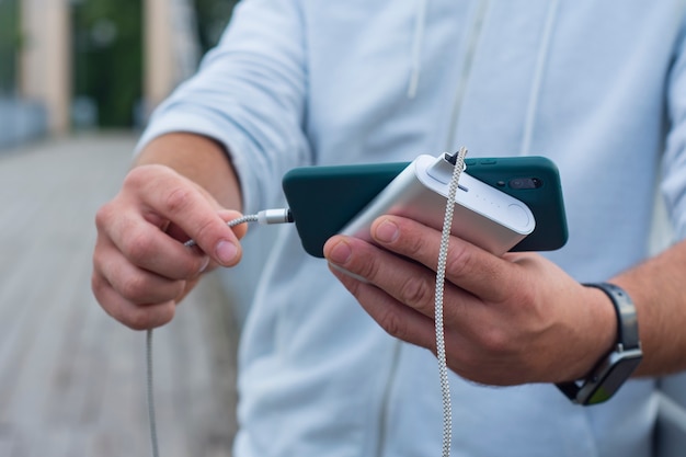 L'uomo carica uno smartphone con un power bank in mano. Caricabatterie portatile per la ricarica di gadget.