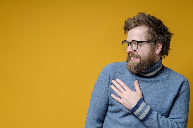 L'uomo carino e modesto tiene la mano sul petto e sorride bonariamente