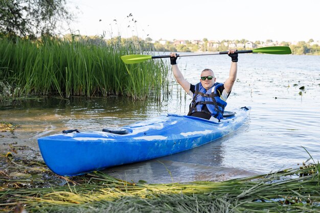 L'uomo caucasico adulto è seduto in un kayak e saluta Il concetto delle attività acquatiche