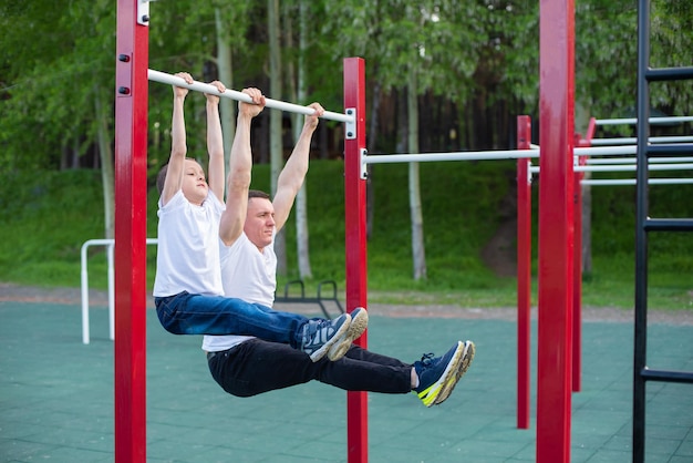 L'uomo caucasico allena un ragazzo sulla barra orizzontale nel parco giochi Papà e figlio praticano sport all'aria aperta