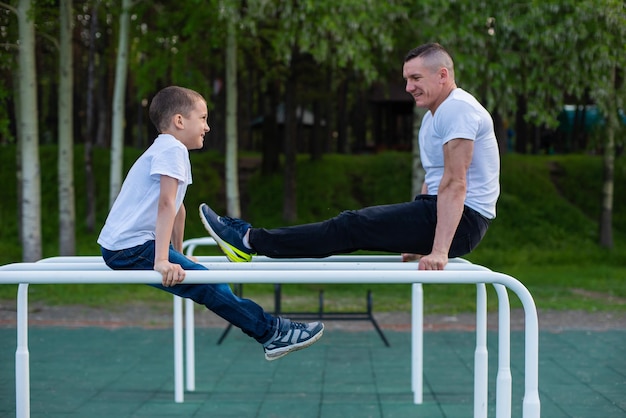 L'uomo caucasico allena un ragazzo sulle sbarre irregolari del parco giochi Papà e figlio praticano sport all'aria aperta