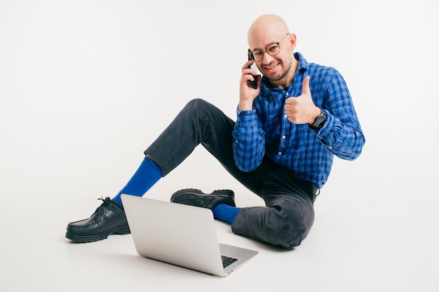 L'uomo caucasico bello senza capelli in camicia blu, pantaloni neri e calzini blu funziona con il computer portatile che mostra il pollice sul gesto.