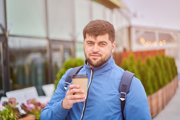 L'uomo caucasico con la tazza di caffè di carta da asporto in mano sta camminando all'aperto