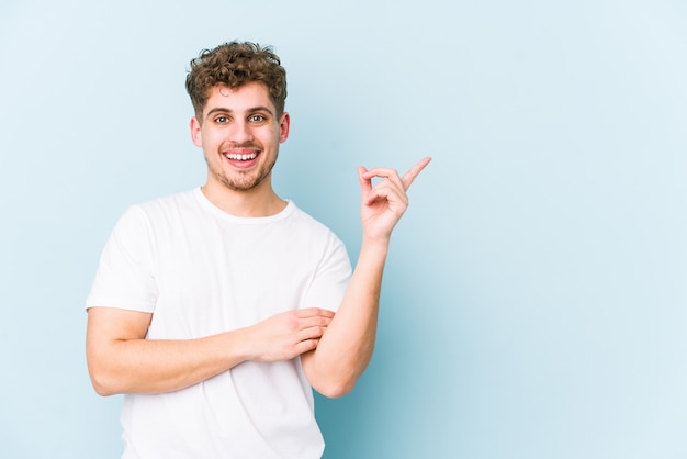 L'uomo caucasico dei giovani capelli ricci biondi ha isolato sorridere indicare allegramente con l'indice via.