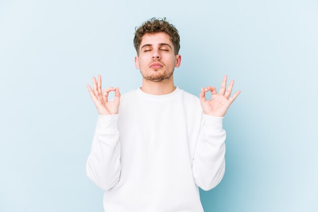 L'uomo caucasico dei giovani capelli ricci biondi isolato si rilassa dopo la dura giornata lavorativa, sta eseguendo l'yoga.