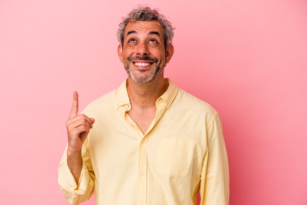 L'uomo caucasico di mezza età isolato su sfondo rosa indica con entrambe le dita anteriori in alto che mostrano uno spazio vuoto.