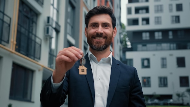 l'uomo caucasico di successo vende la proprietà della casa tenendo le chiavi dal nuovo appartamento in un edificio moderno della città