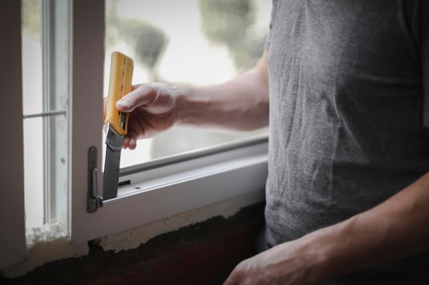 L'uomo caucasico pulisce il telaio di una finestra con un coltello da costruzione