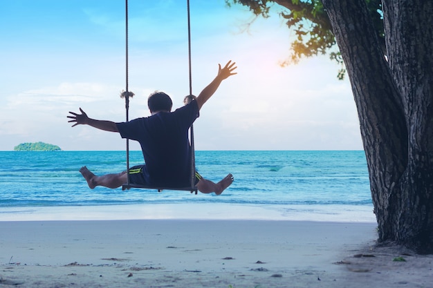 L'uomo celebra la libertà sull'altalena in spiaggia. Viaggio di vacanze estive.