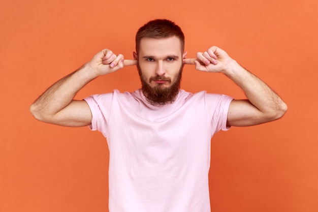 L'uomo che chiude le orecchie con le dita guardando seriamente la fotocamera stanco del rumore irritato vuole il silenzio