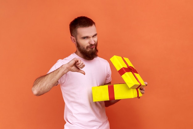 L'uomo che disimballa il presente per sapere cosa ha ricevuto essendo frustrato e deluso mostrando il pollice in giù