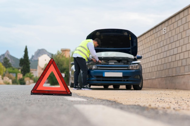 L'uomo che indossa un giubbotto riflettente guarda il cofano della sua auto