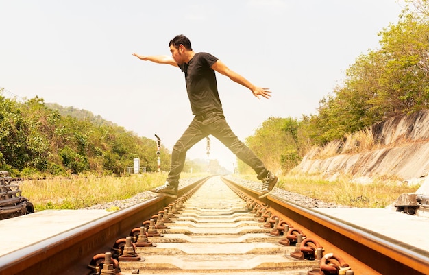 L'uomo che indossa una camicia nera allarga le mani e cammina sui binari del treno