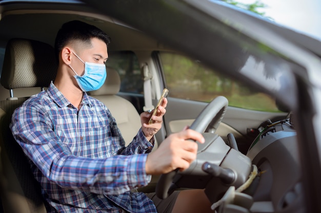 L'uomo che indossa una maschera, premere il cellulare sull'auto. Un uomo che guarda il telefono durante la guida.