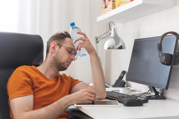 L'uomo che lavora a casa soffre di caldo e sete si raffredda con una bottiglia d'acqua nelle calde giornate estive