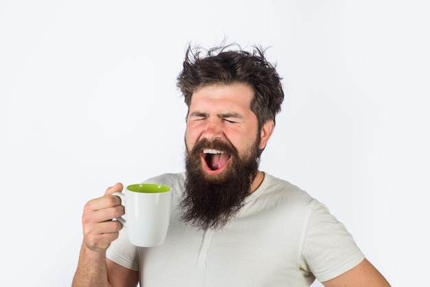 L'uomo che sbadiglia con la faccia assonnata cerca di svegliarsi con una tazza di caffè uomo tiene una tazza con una bevanda calda uomo con