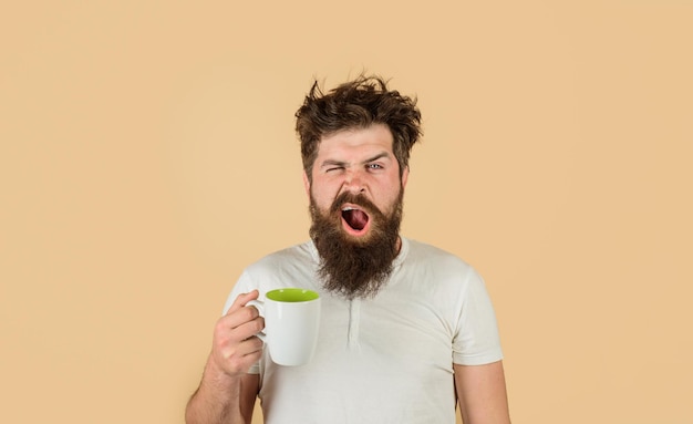 L'uomo che sbadiglia con la faccia assonnata cerca di svegliarsi con una tazza di caffè uomo tiene una tazza con una bevanda calda uomo con