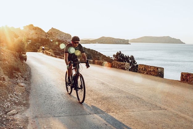 L'uomo ciclista pedalando su una bici da strada all'aperto nel tramonto sulla strada costiera