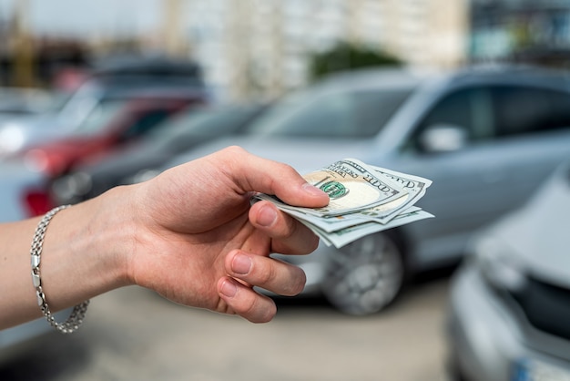 L'uomo compra un'auto moderna, tenendo il dollaro contro l'auto nel retro. concetto di vendita