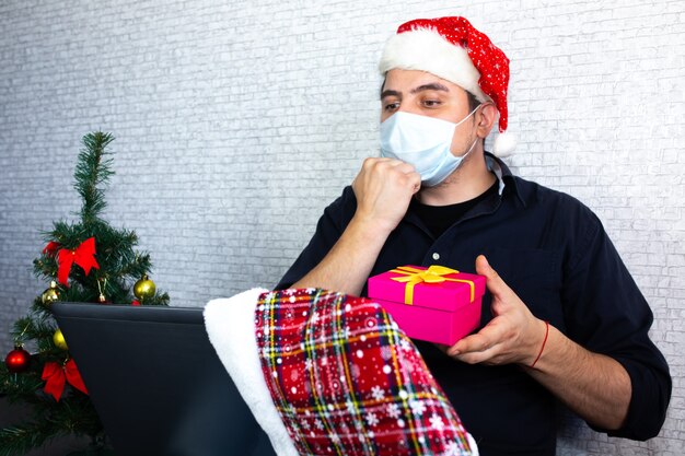 L'uomo comunica tramite il linguaggio dei segni. Il ragazzo con il cappello da Babbo Natale vicino al laptop sta interagendo tramite videochiamate. Vivi con la disabilità. Natale in isolamento a casa. Distanziamento sociale per le vacanze.