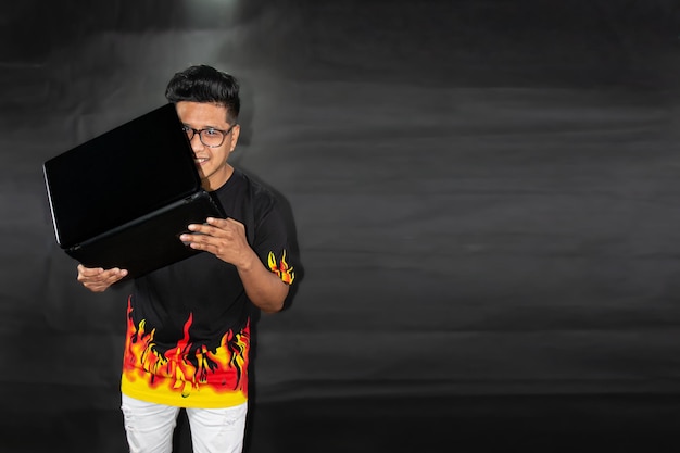 L'uomo con gli occhiali e la polo con le fiamme tiene un laptop. Concetto di tecnologia su sfondo nero