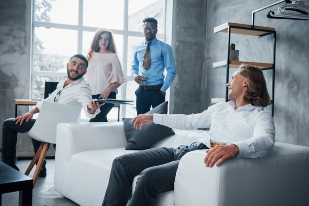 L'uomo con i capelli corti vuole condividere i suoi risultati con un altro ragazzo. Gruppo di impiegati multirazziali in abiti formali parlando di compiti e piani