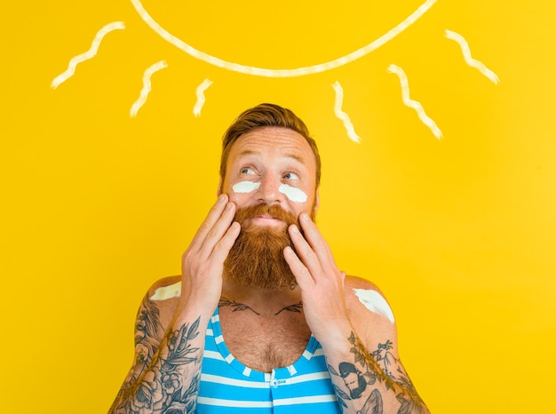 L'uomo con i tatuaggi e il costume da bagno si mette la crema solare