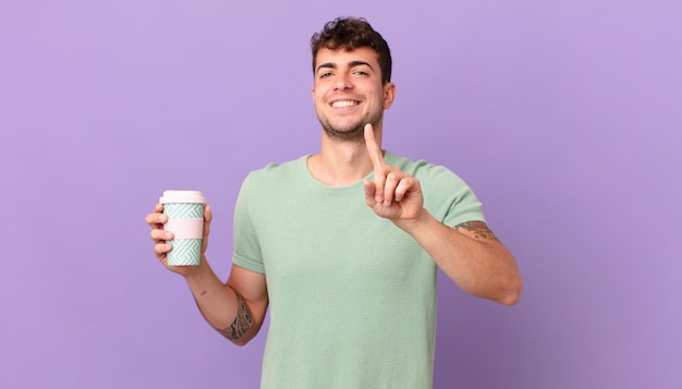 L'uomo con il caffè sorride con orgoglio e fiducia mentre fa la posa numero uno in modo trionfante, sentendosi un leader