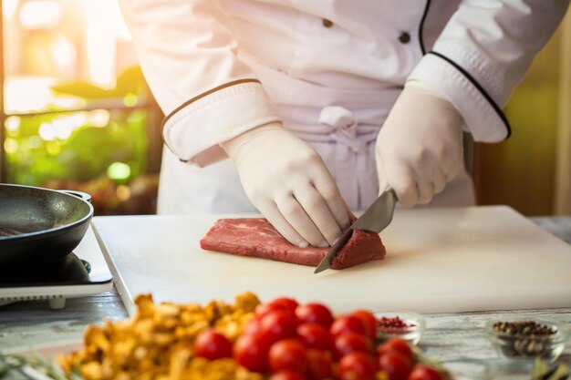 L'uomo con il coltello taglia la carne. Tavola da cucina bianca sul tavolo. Vitello fresco per una bistecca. Lavoro di chef.