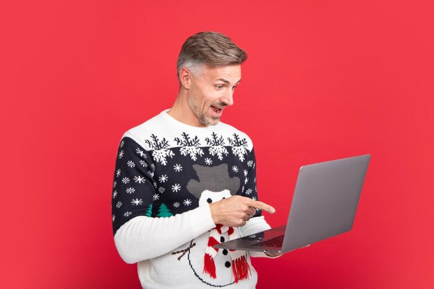 L'uomo con il computer portatile L'uomo in maglione di Natale e cappello da Babbo Natale su sfondo rosso