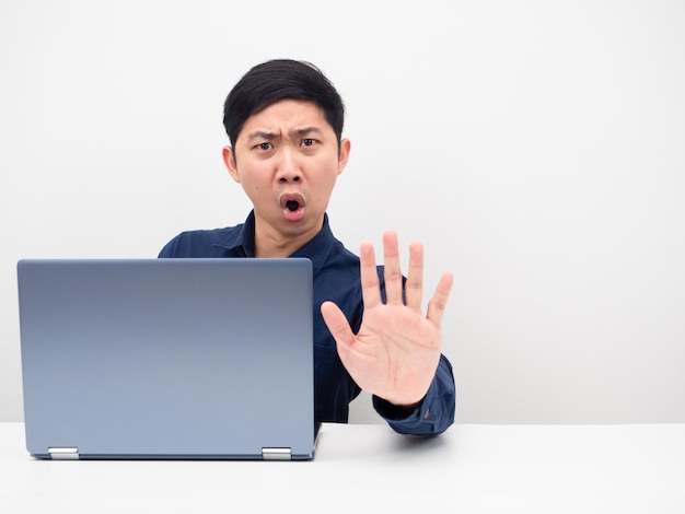 L'uomo con il computer portatile sul tavolo mostra la mano per fermare lo spazio della copia del viso arrabbiato sfondo bianco