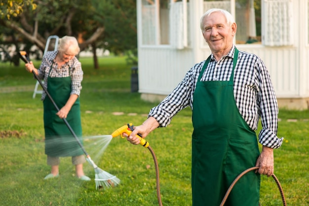 L'uomo con il tubo da giardino sorridente maschio anziano in grembiule all'aperto trova lavoro nel giardinaggio