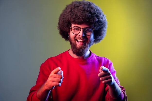 L'uomo con l'acconciatura afro che punta alla telecamera sorridente facendo una scelta felice abbiamo bisogno di te