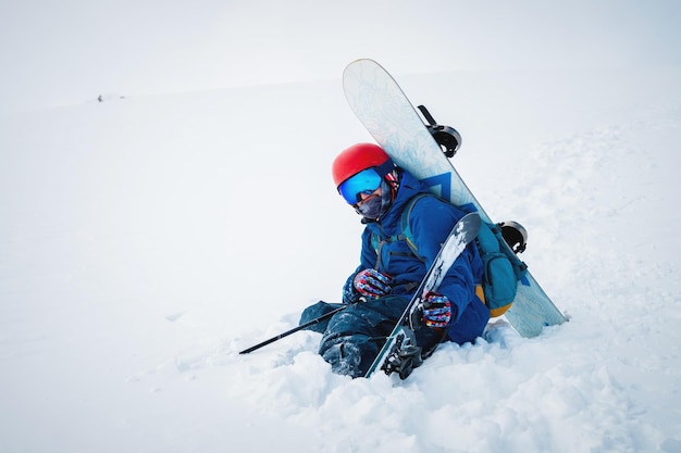 L'uomo con l'attrezzatura da sci e uno snowboard è seduto in una montagna innevata cielo blu e montagna innevato in