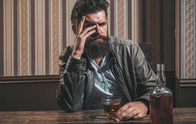 L'uomo con la barba tiene il brandy di vetro L'uomo con in mano un bicchiere di whisky L'uomo barbuto bello ed elegante sta bevendo a casa dopo il lavoro Uomo ubriaco