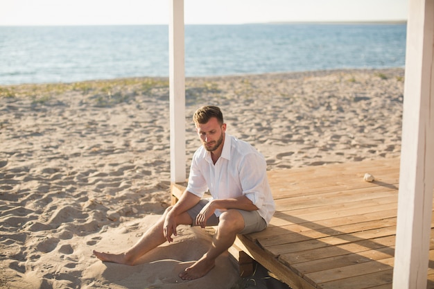 L'uomo con la camicia bianca e pantaloncini seduto sulla spiaggia