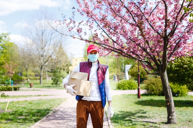 L'uomo con la maschera facciale sta consegnando cibo e generi alimentari durante l'epidemia di virus.