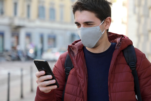 L'uomo con la maschera protettiva guarda il suo smartphone in strada