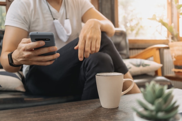 L'uomo con la maschera sta usando lo smartphone e beve il caffè al bar