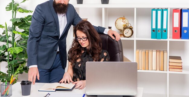 L'uomo con la vista del raccolto si trova sopra una seria ragazza in carriera che lavora alla scrivania dei compagni di lavoro