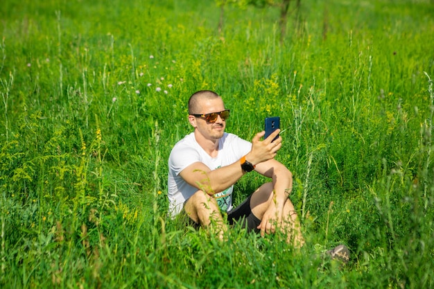 L'uomo con lo smartphone e in occhiali da sole sorride. Fare selfie in un luogo rurale