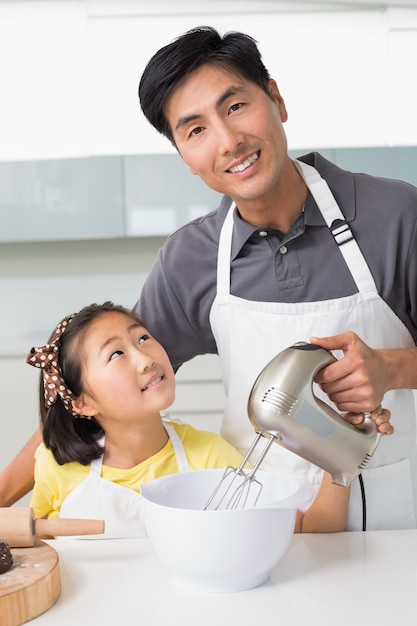 L&#39;uomo con sua figlia utilizzando la frusta elettrica nella ciotola in cucina