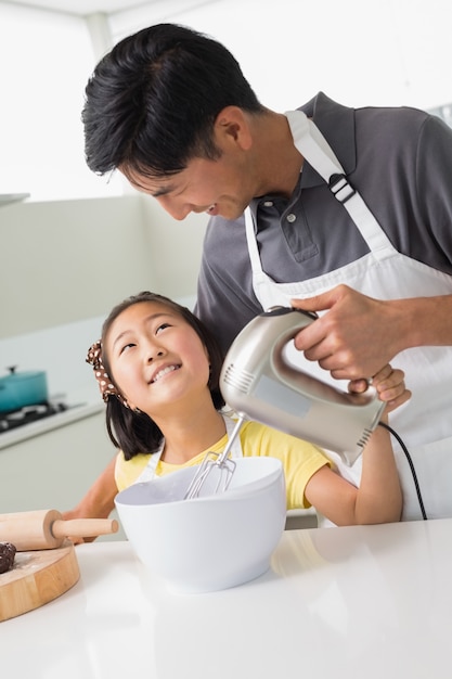 L&#39;uomo con sua figlia utilizzando la frusta elettrica nella ciotola in cucina