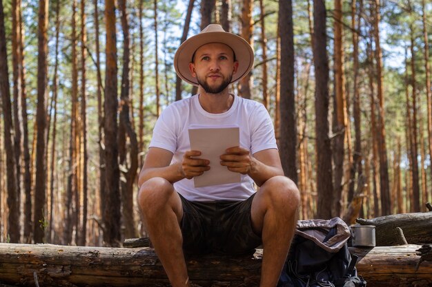 L'uomo con un cappello tiene una mappa nelle sue mani durante un viaggio in campeggio. Escursione in montagna, foresta.