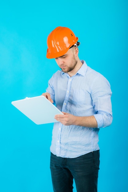 l'uomo con una camicia blu con un casco protettivo arancione e un taccuino bianco si trova su sfondo blu