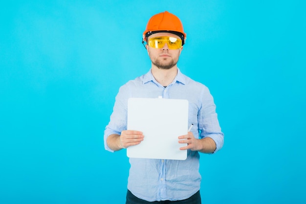 l'uomo con una camicia blu con un casco protettivo arancione e un taccuino bianco si trova su sfondo blu