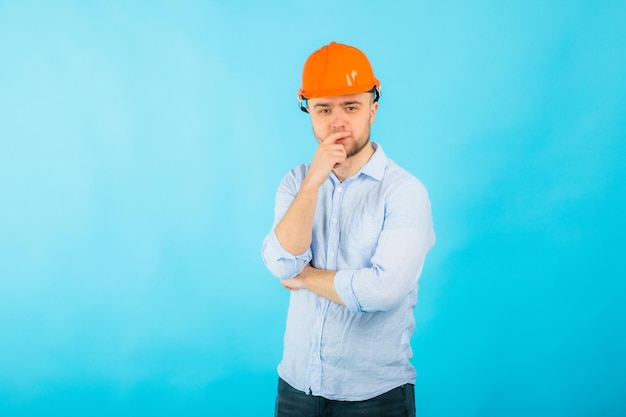 l'uomo con una camicia blu con un casco protettivo arancione e un taccuino bianco si trova su sfondo blu