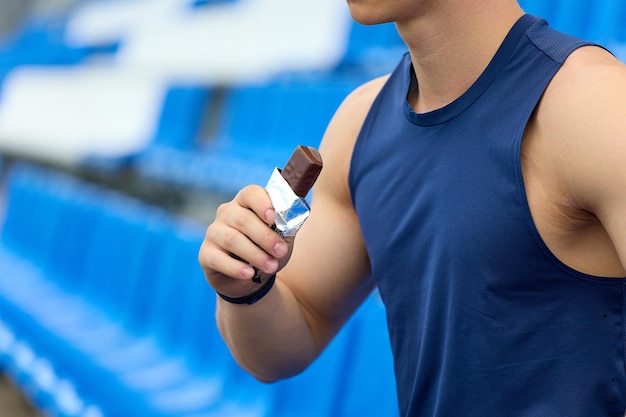 L'uomo con una maglia sportiva blu riposa nello stand per i fan che mangiano una barretta di cioccolato